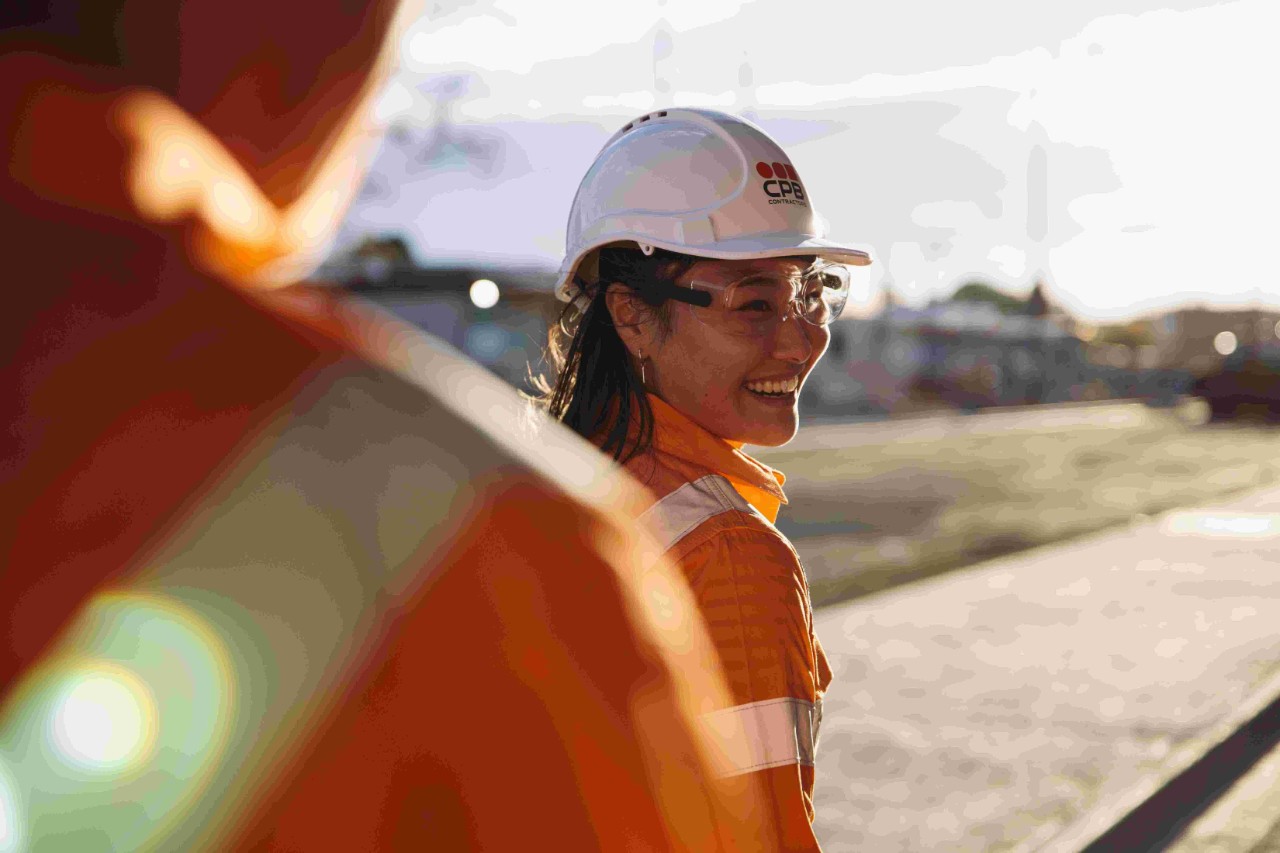 Construction workers smiling as she walks towards a sunset