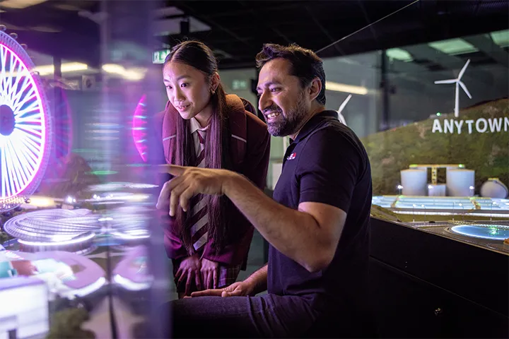 TAFE NSW teacher points out features of an illuminated sustainable town model to a student.