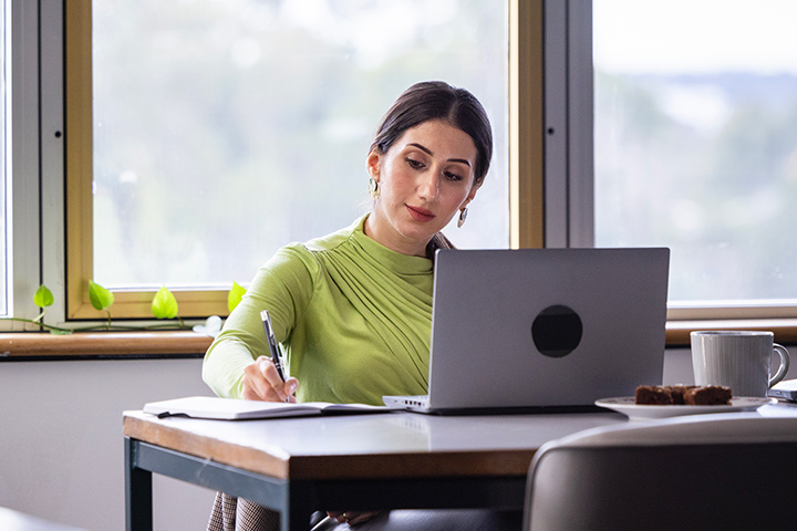 Tourism and travel management teacher leads a group of students on an outdoor field tour, standing near an iron fence while referencing notes on a clipboard as students listen and observe.