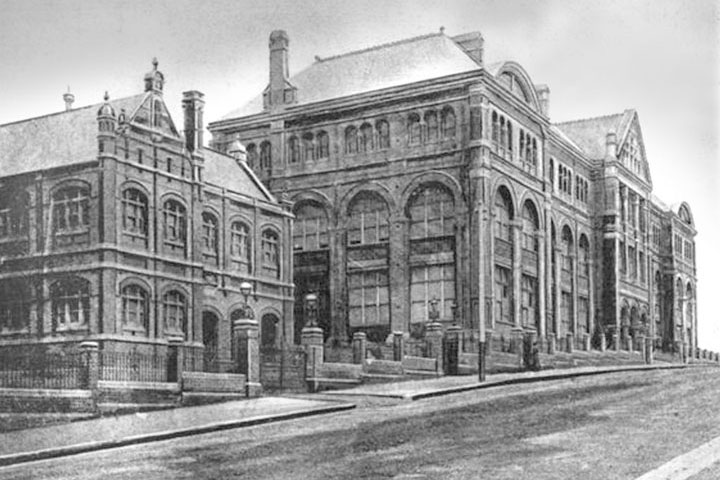 Historic building with arched windows on a sloped street, featuring stone details and vintage fencing.