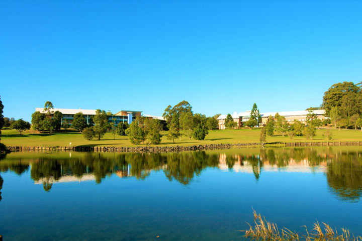Photo of the Coffs Harbour Education Campus showing a lake surrounded by grass with the campus buildings in the background.