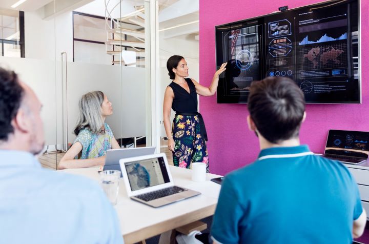 A woman presents to an audience, engaging them with her speech and presentation slides in a professional setting.