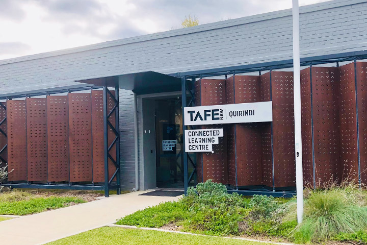 Entrance of the TAFE NSW Quirindi Connected Learning Centre featuring modern grey and rust-coloured panels, with signage above the doorway and a landscaped lawn with greenery.