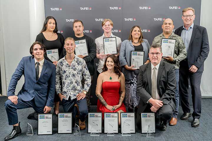 A group of Aboriginal and Torres Strait Islander people stand and kneel holding their awards for their high achievements.