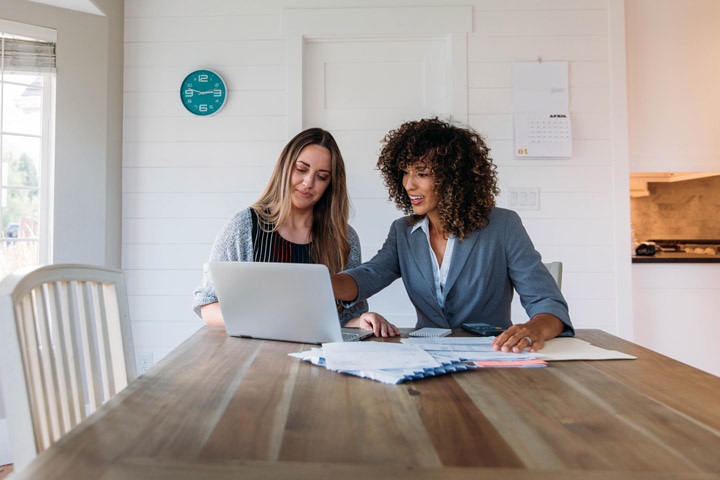 Female mortgage broker in a professional setting, discussing mortgage options with a client seated next to her at a desk.