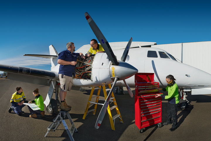 Hands-on aviation education: Teacher guiding students on a tarmac, collaboratively working on the maintenance of a small plane for practical learning.