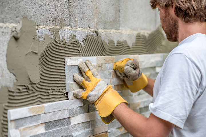A tiler skillfully installs tiles on an outdoor wall, carefully aligning each piece by hand.