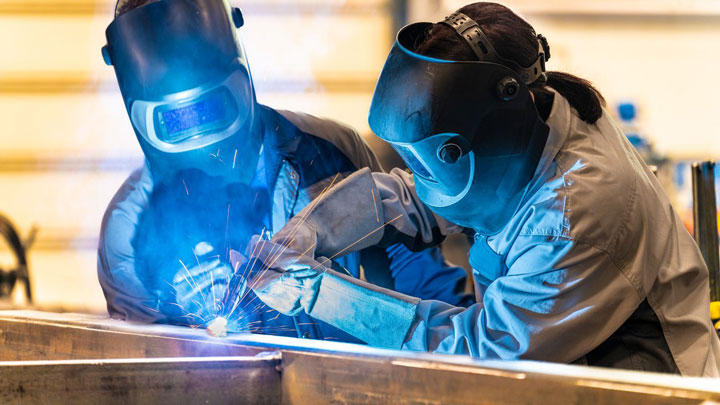 Two welders wearing full protective gear work on a project.