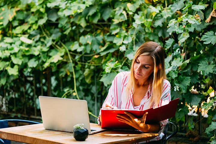 Woman working outside with her laptop and book.