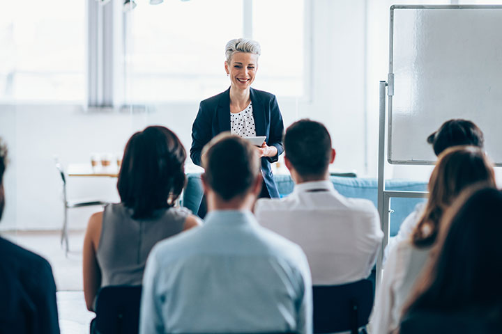Woman giving a presentation about Work Health and Safety to a group of attentive people in a room.