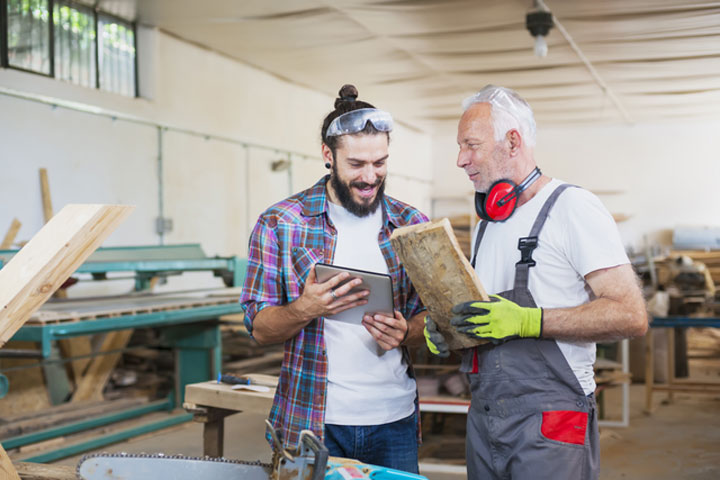 A senior carpenter works alongside a young apprentice.