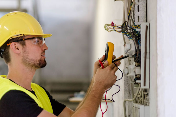 A man wearing protective gear tests an electronics board with specialized equipment in a controlled environment.