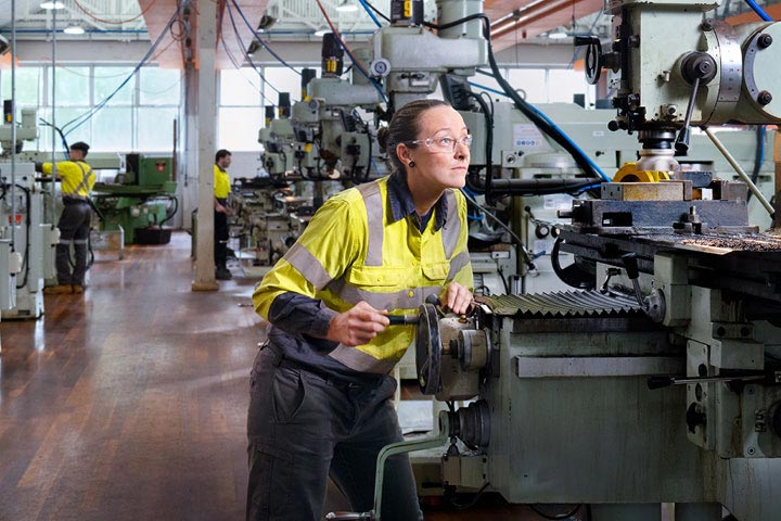 A woman wearing safety gear operates machinery in an industrial workshop.