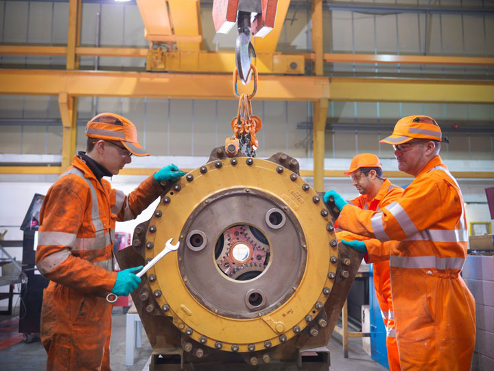 Workers in high-visibility clothing use tools and a crane to lift heavy goods in a busy work environment.