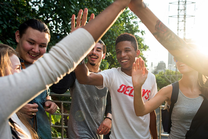 A diverse group of young men and women standing in a circle in sunshine and ‘high-fiving’