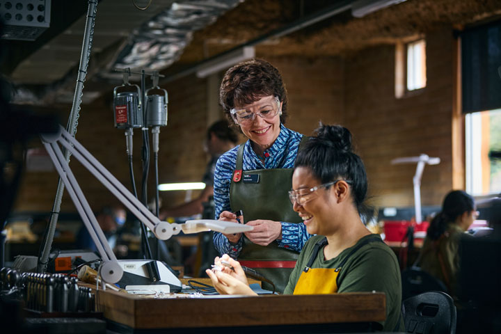 A teacher guides a student working with tools under a light in a workshop.