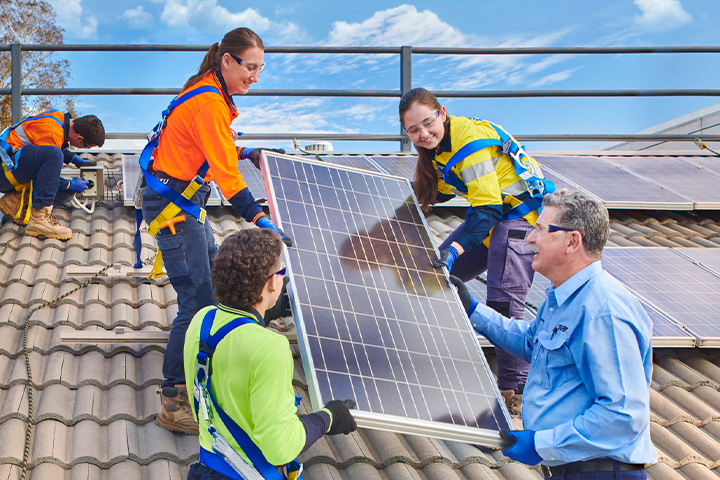 A teacher guides students as they install solar panels on a school roof.