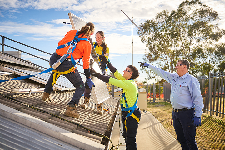 Teacher instructing three students in the installation of solar panels on a rooftop