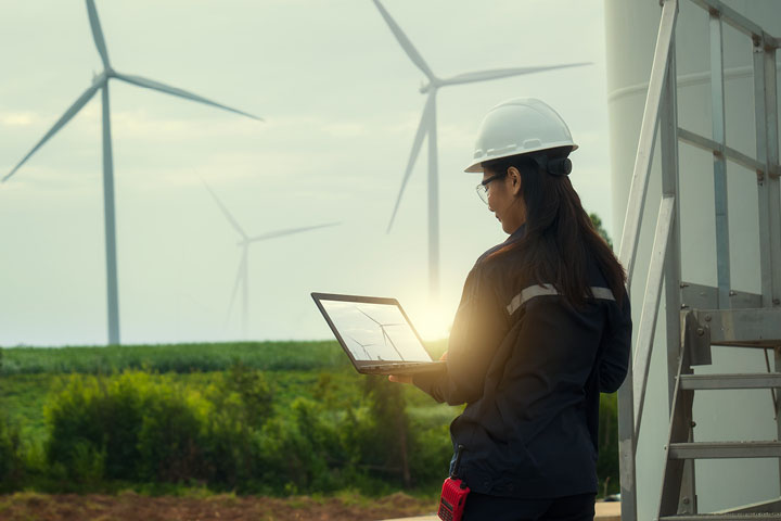 Young female engineer reviewing wind turbine data on laptop.