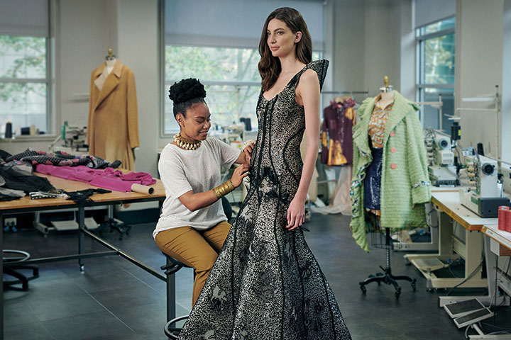 A young female fashion designer carefully adjusts her creation on a model.