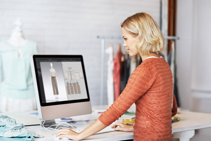 A young female fashion designer reviews her designs on a Mac computer.