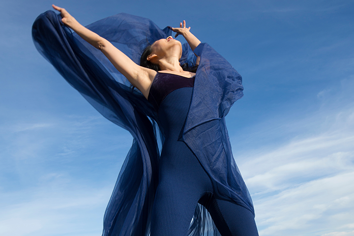 A woman poses while looking up at a clear blue sky.