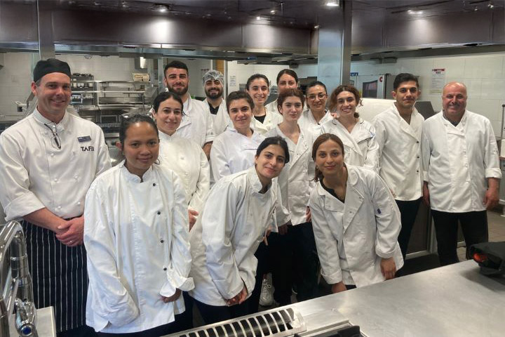 Hospitality students in chef uniforms pose for a photo in a commercial kitchen.