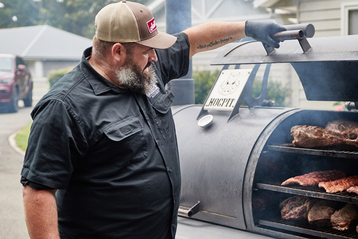 A BBQ pitmaster tends to a large smoker.