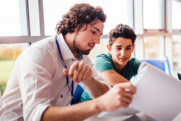 A TAFE NSW young male counsellor sits with a male student. They’re looking at documents together.