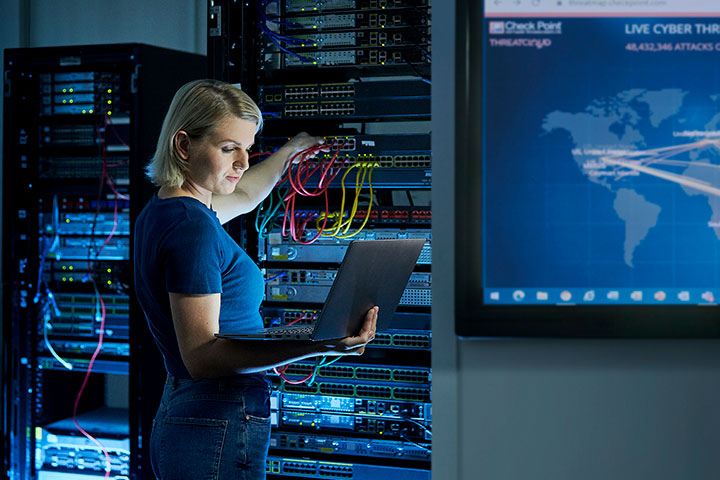 Female network engineer working on a server and holding a laptop