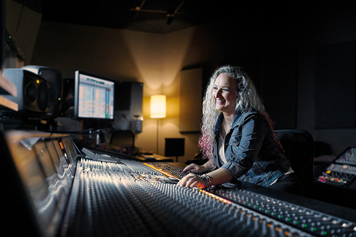 Student sound engineer working alone at a mixing console/soundboard in a professional recording studio.