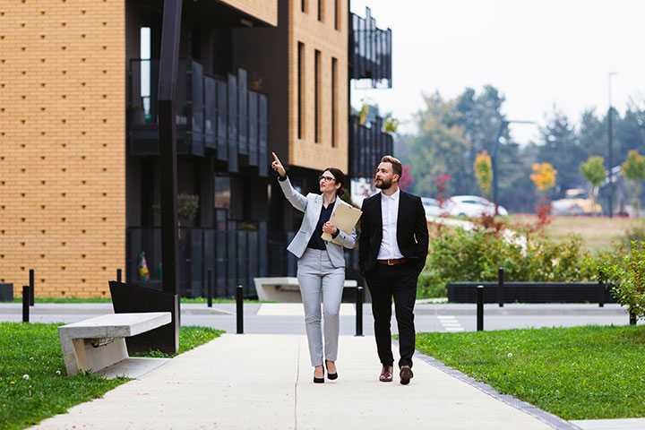 A pair of real estate agents, one male and one female, both wearing suits, walking through an area and assessing potential properties.