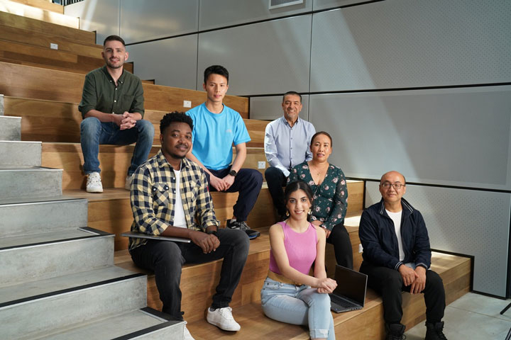 A group of seven people are posing for a photo sitting on different steps of a set of stairs. They are all from different backgrounds.
