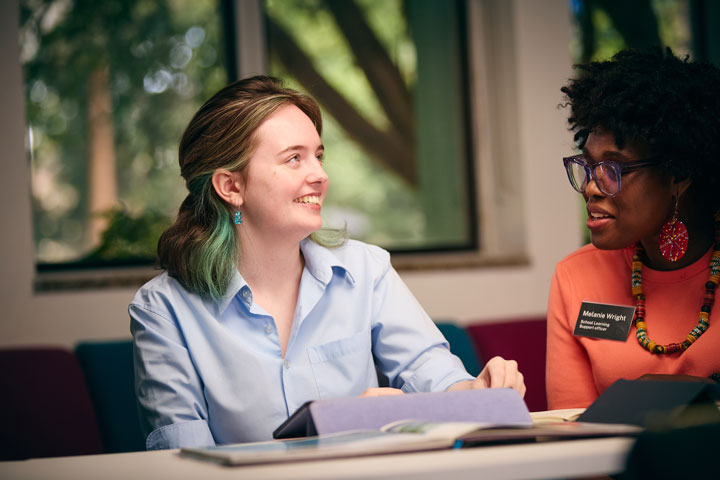 Student with blue hair and a learning support officer looking at a tablet together.