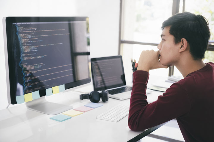 A man working at a desk, engaged with a computer screen and surrounded by office supplies.