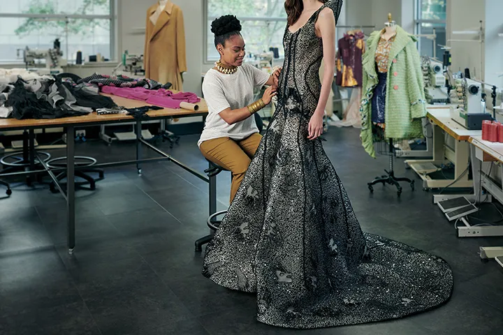 A young female fashion designer adjusts a garment on a model.