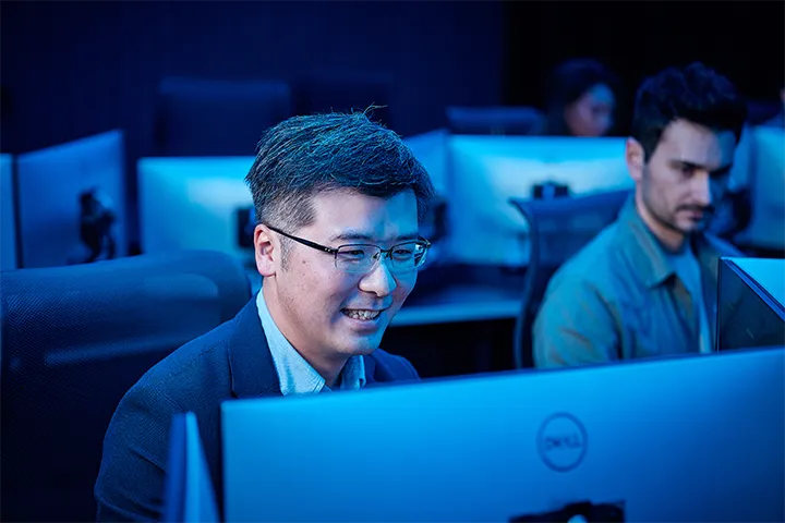 A TAFE NSW student engaged in a cyber defence class, smiling behind a computer screen. Other students do the same around him.
