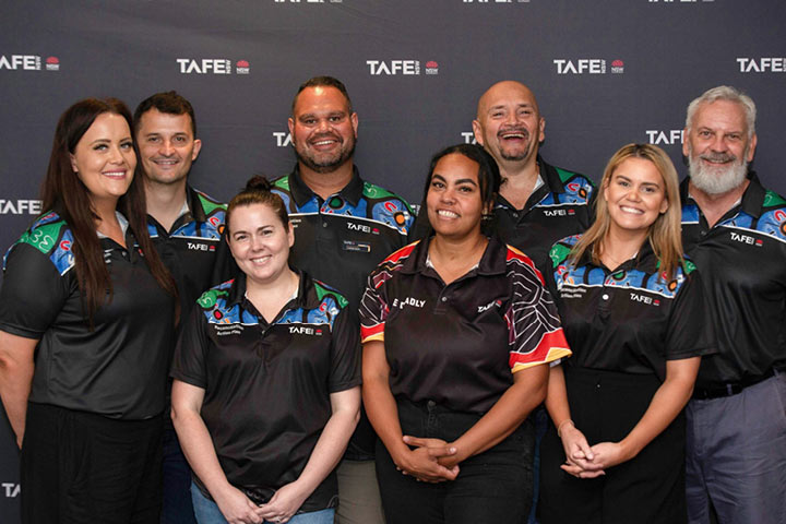 A group of eight Aboriginal ɫֱemployees smiling to the camera and wearing ɫֱshirts with a range of colourful Indigenous designs.