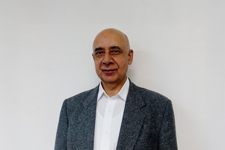 Dr. Amir Christi, Head Teacher of Information Technology at TAFE NSW, smiles knowingly at the camera. He is sharply dressed in a crisp white shirt and a charcoal tweed blazer with notched lapels.
