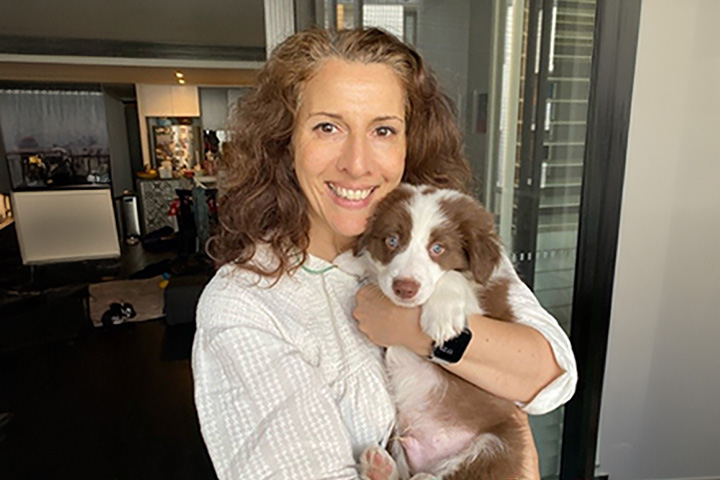 TAFE NSW English teacher Maria Mitrofanis smiles widely at the camera, wearing a white blouse and holding a Border Collie puppy.