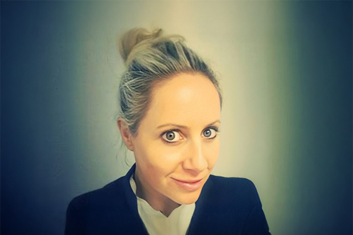 TAFE NSW Ultimo campus Beauty and Makeup teacher Trina Storey-Hollis is dressed in a polished white shirt and a classic black blazer. Her blonde hair is styled in an elegant top knot bun.