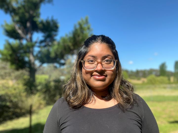 Raya Shanum, a graduate of TAFE NSW Armidale, smiles confidently. She stands outdoors, in a field.