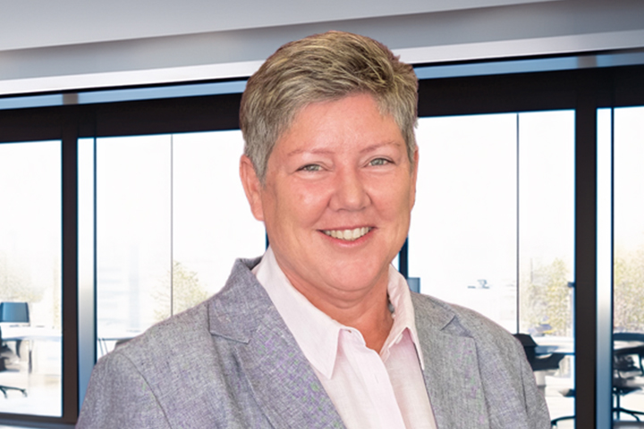 The image shows Megan Callinan in a grey blazer worn over a white collared shirt . She has short, light hair and is smiling.