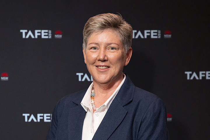 The image shows Megan Callinan in a grey blazer worn over a white collared shirt . She has short, light hair and is smiling.