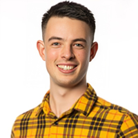 A headshot image of Aidan Williams smiling at the camera. He is wearing a bright yellow and black tartan shirt.