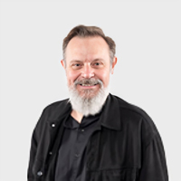 A headshot image of Craig Daalmeijer-Power smiling at the camera. He is wearing a black collared shirt and has a grey beard.