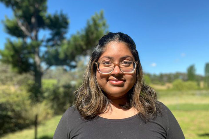 Raya Shanum, a graduate of TAFE NSW Armidale, smiles confidently. She stands outdoors, in a field.