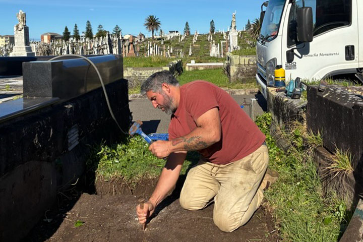 Daniel Fuentes kneeing on the floor, hammering a large nail into the ground.
