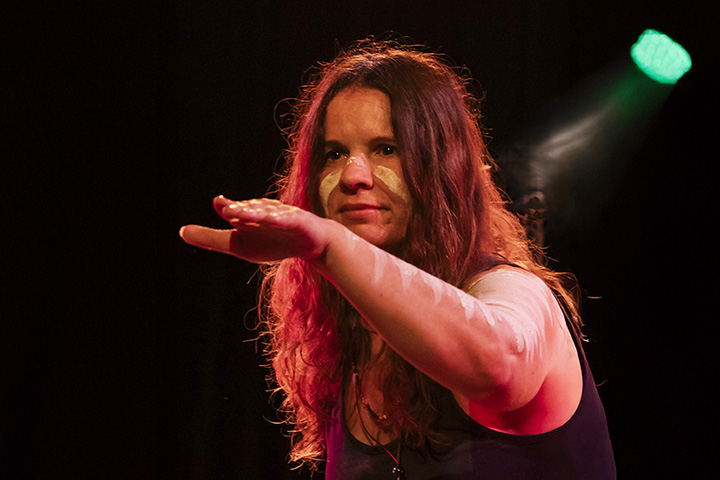 Elizabeth (Murrah) Keys, proud Worimi woman and head teacher at TAFE NSW Eora, performs a traditional dance. She holds her arm out, wears a traditional necklace and has paint markings on her face and arm.