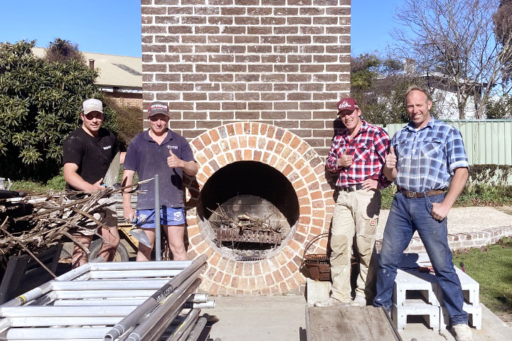 Bruce, Max, Barry and their dad Jobe Harkness smile and give thumbs up in front of a brick fireplace they built together.
